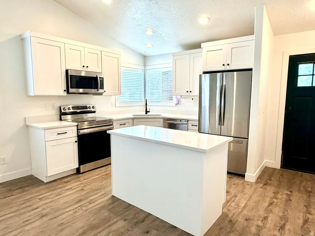 Kitchen featuring white shaker cabinetry, stainless steel appliances, a center island, light countertops, and wood-finish flooring