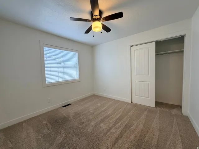 Bright secondary bedroom featuring neutral carpeting, a ceiling fan with integrated lighting, and a spacious walk-in closet with bifold doors and shelving