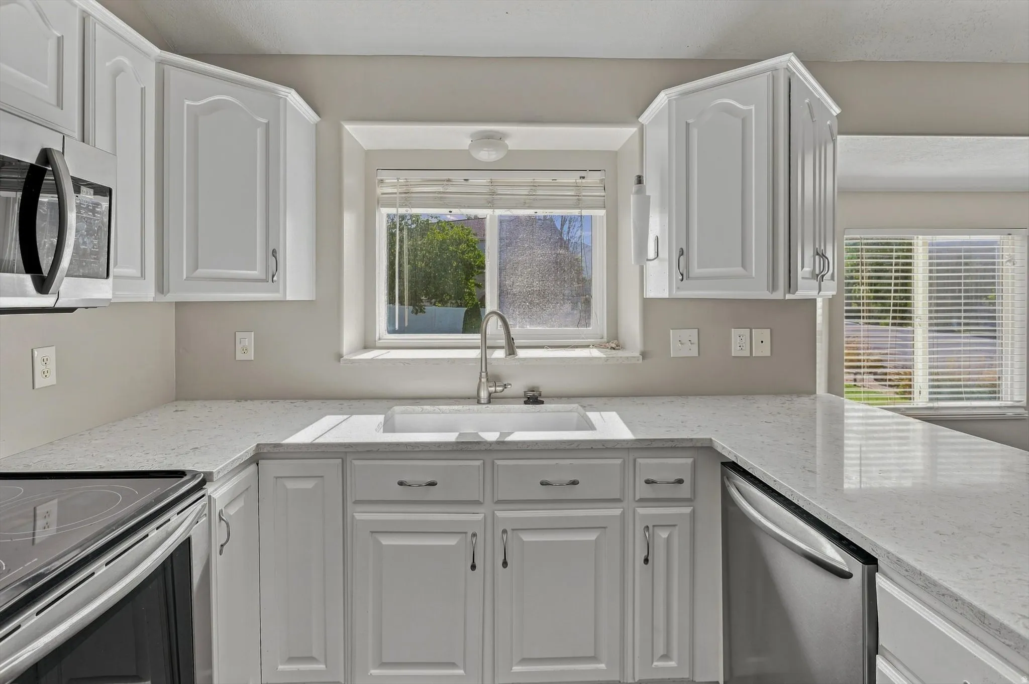 White cabinetry with brushed nickel hardware, stainless steel appliances, a double basin sink, and light-toned countertops