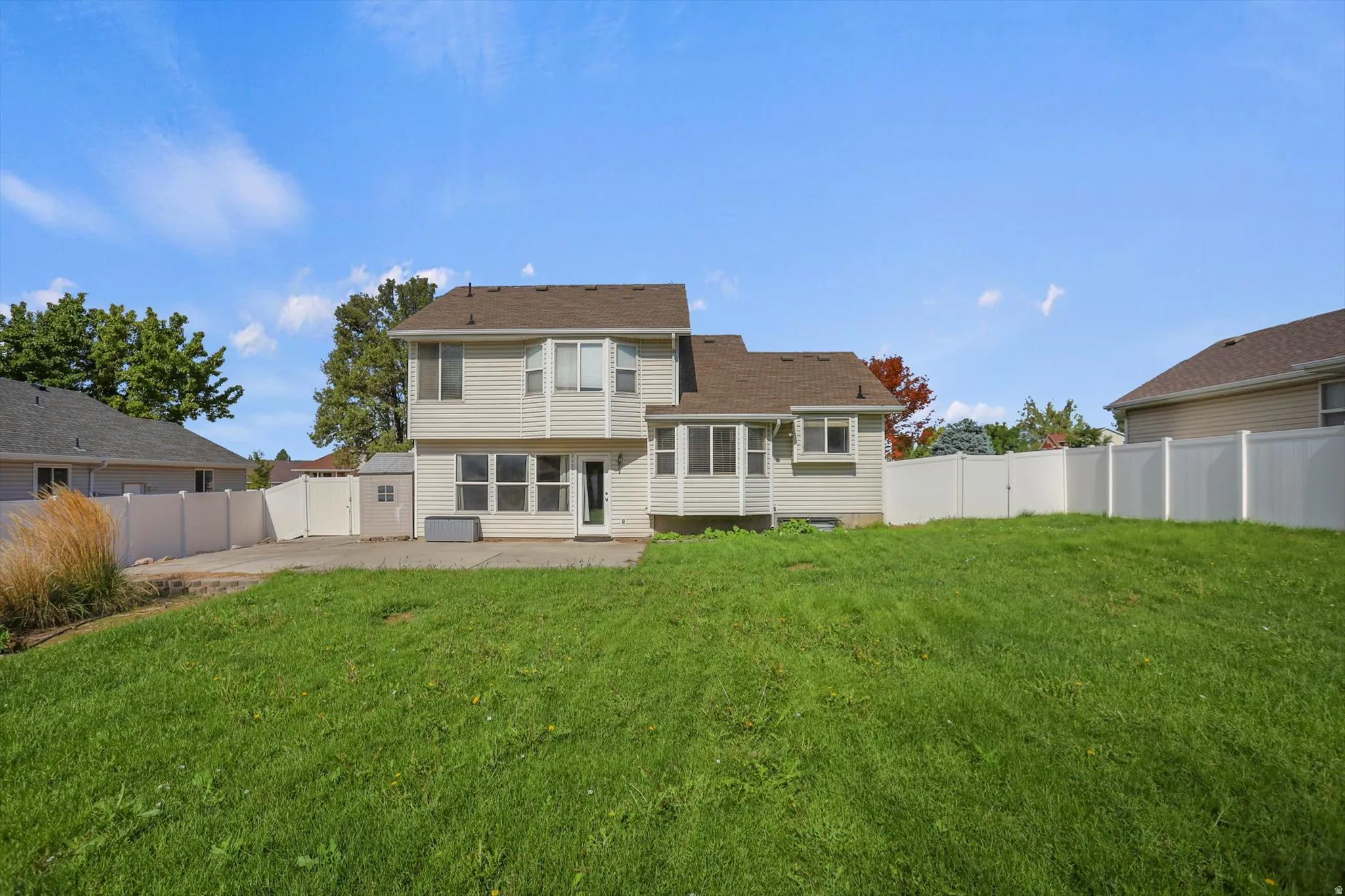 Expansive backyard featuring a manicured lawn, concrete patio, and white privacy fencing