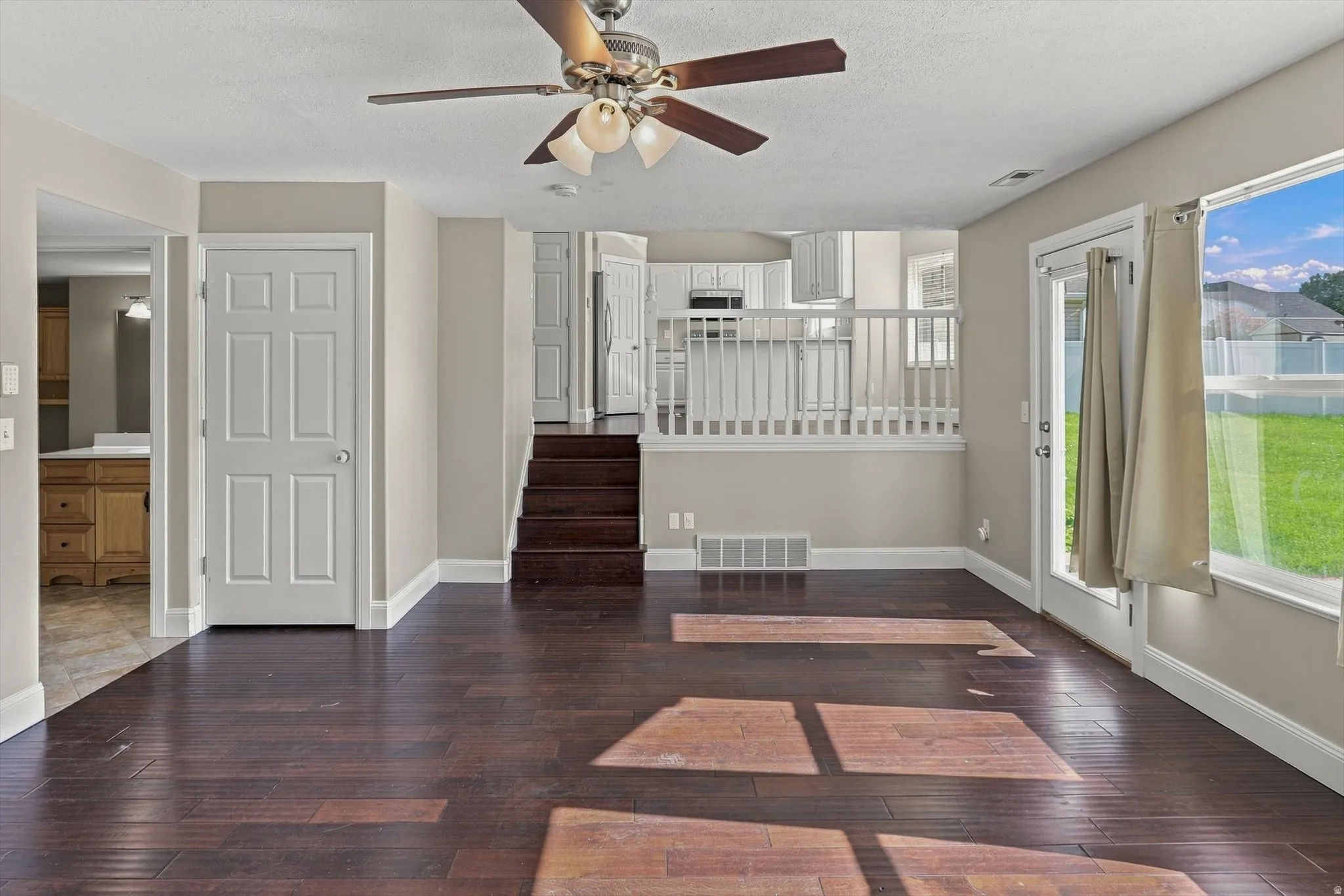 Dark wood-finish flooring, white trim, ceiling fan light fixture, white interior doors, and a glass-paneled exterior door