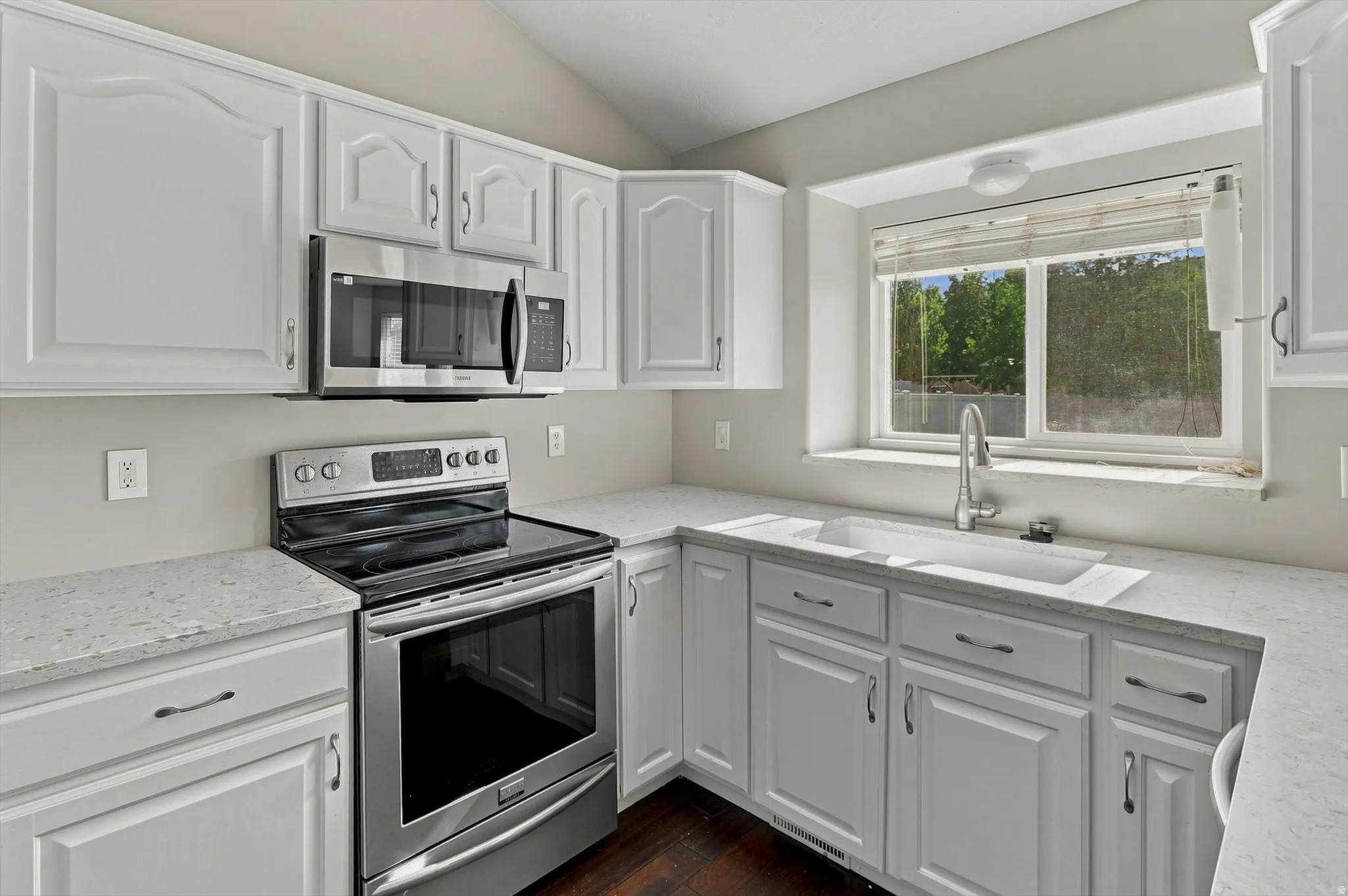White cabinetry, stainless steel appliances, solid surface countertops, and a single basin sink