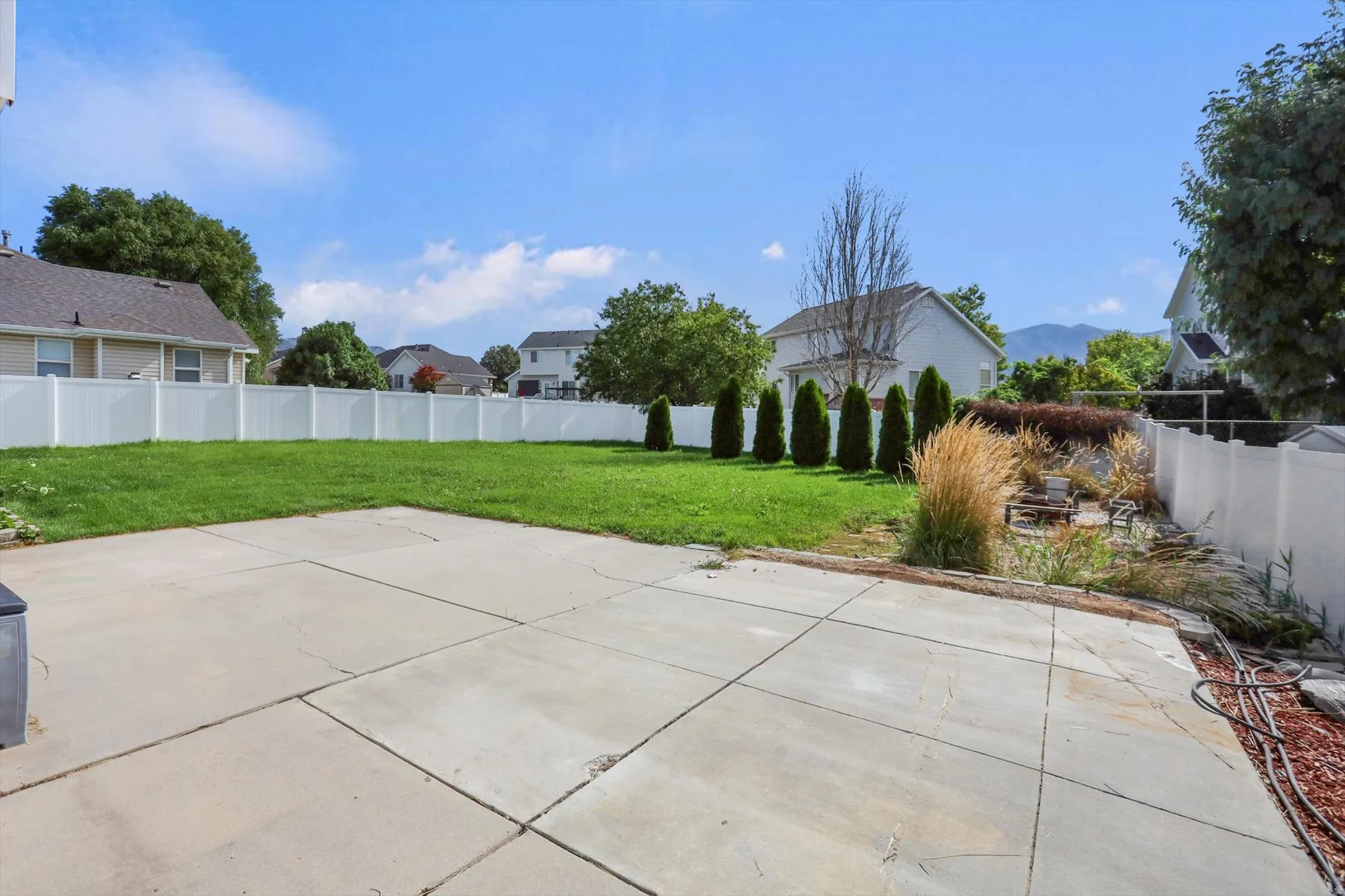 Expansive concrete patio with a lush green lawn, private vinyl fencing, and mature landscaping