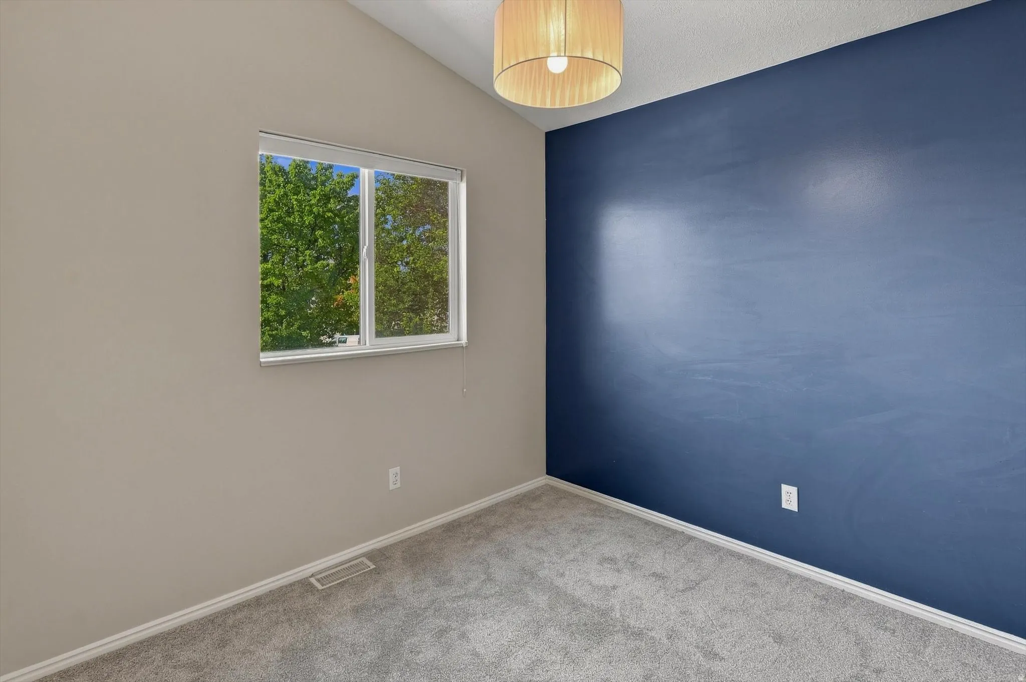 Vaulted ceiling with a drum pendant light, two-tone wall paint, window with white trim, and gray carpeting