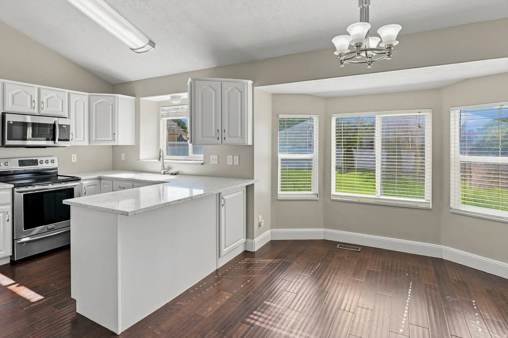 Vaulted ceiling kitchen featuring white cabinetry, stainless steel appliances, and a peninsula with a light-toned countertop