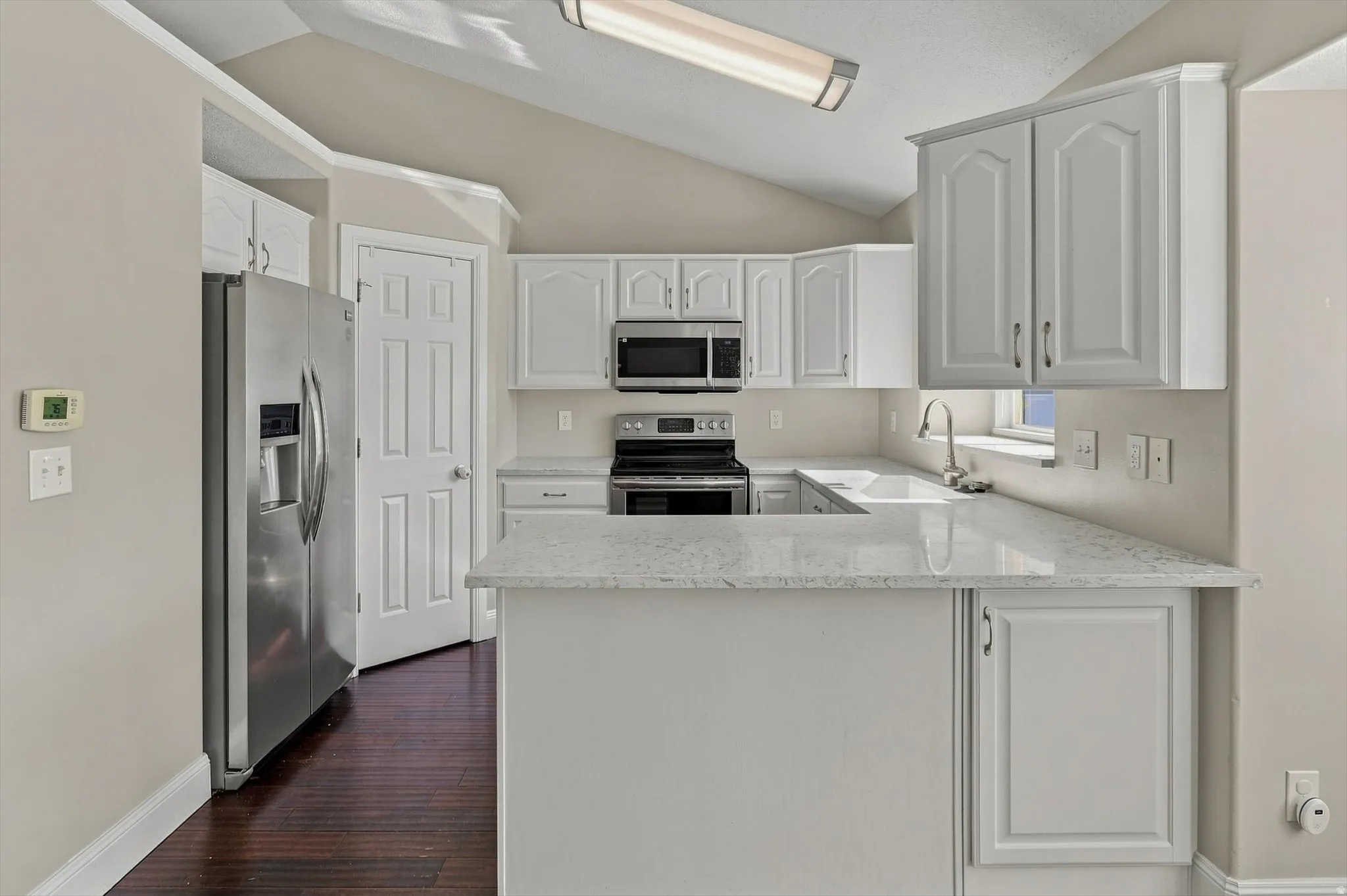 Kitchen featuring light-toned cabinetry, light-toned countertops, a stainless steel refrigerator, and a built-in stainless steel microwave and range