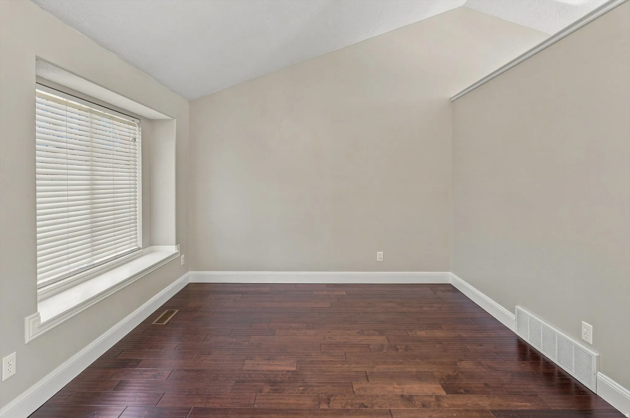Vaulted ceiling, wood-finish flooring, neutral wall tones, and a window with a deep sill