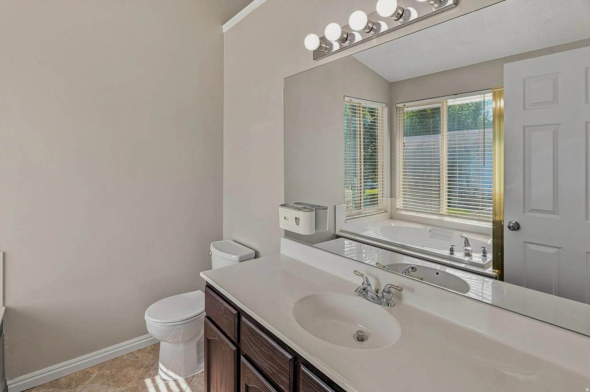 Vanity with an integrated sink and chrome faucet, wood-finish cabinetry, full-width mirror, and a built-in bathtub with multiple windows