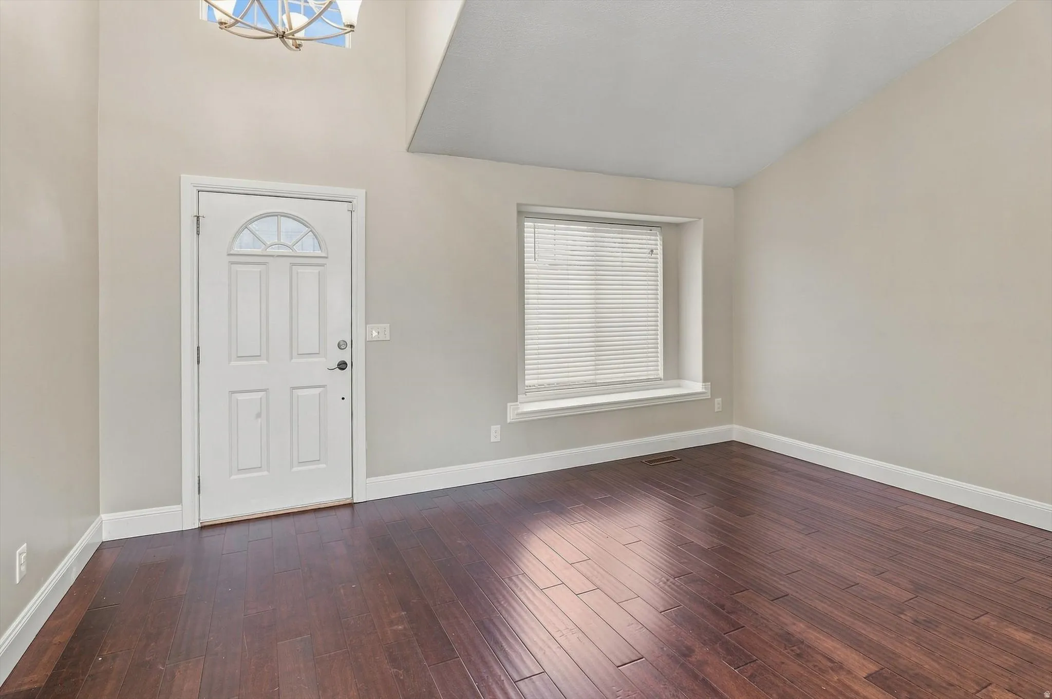 Hardwood-finish flooring throughout, a vaulted ceiling, and a prominent front entry door with an arched window accent