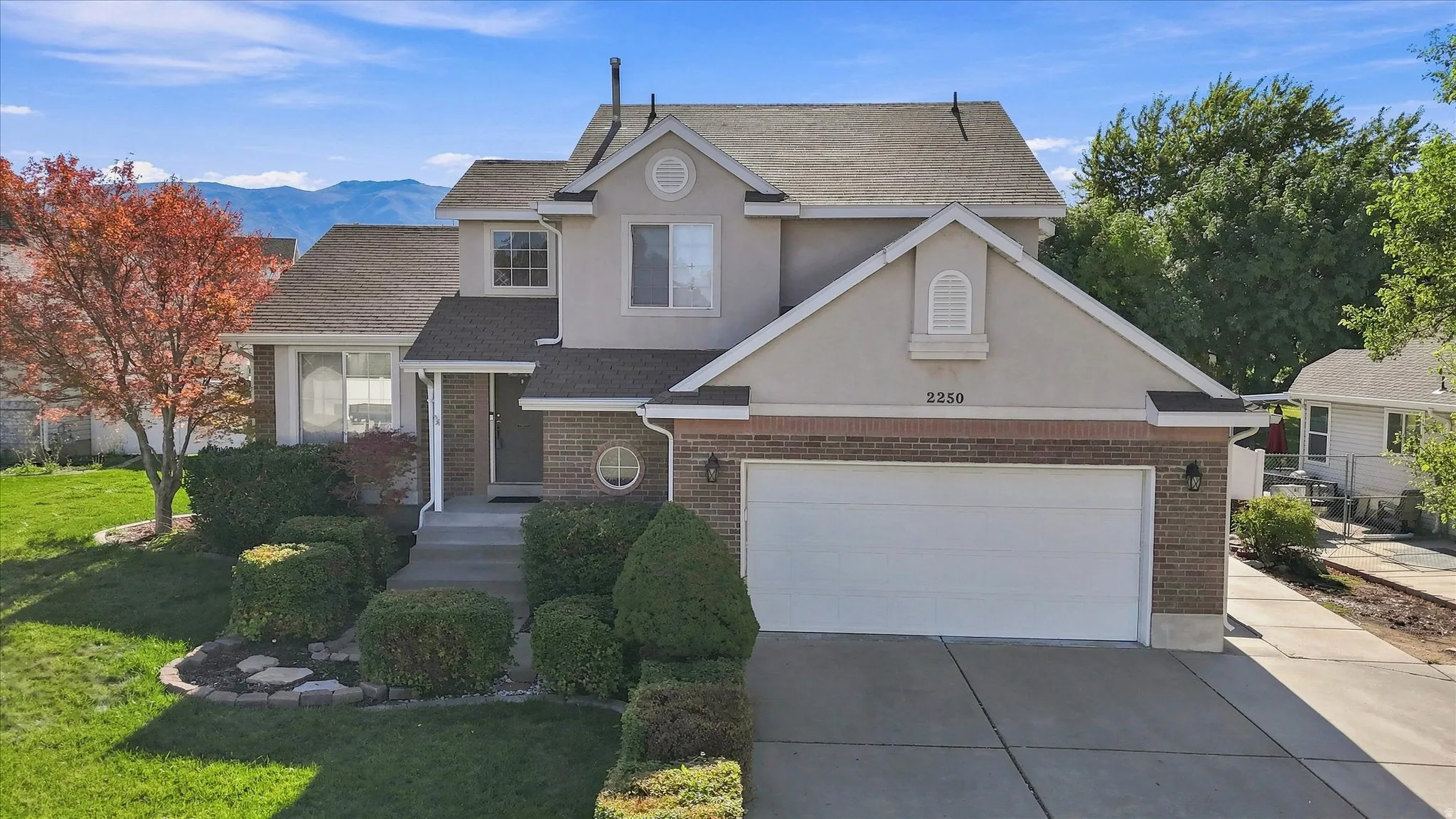 Stucco and brick exterior with a prominent two-car garage, established landscaping, and a central entryway