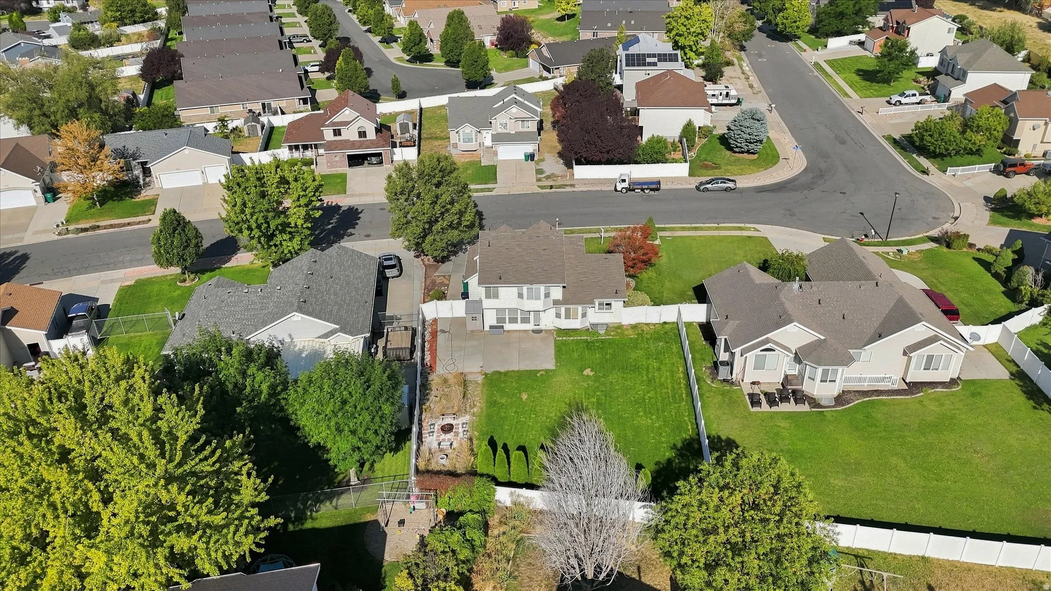 Expansive residential property with a large backyard featuring a manicured lawn, white fencing, and surrounding mature trees