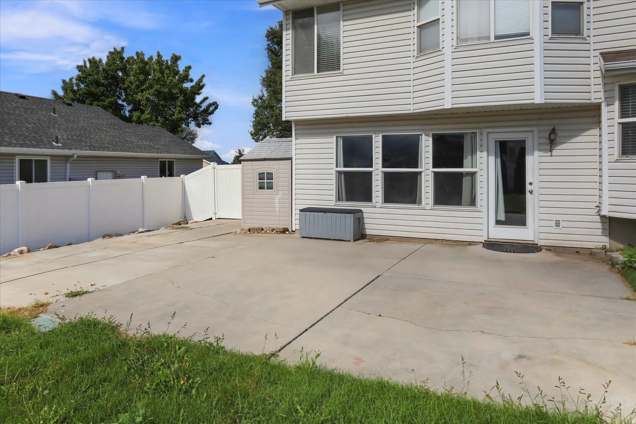 Expansive concrete patio with direct access to interior, featuring multiple windows, and a storage shed