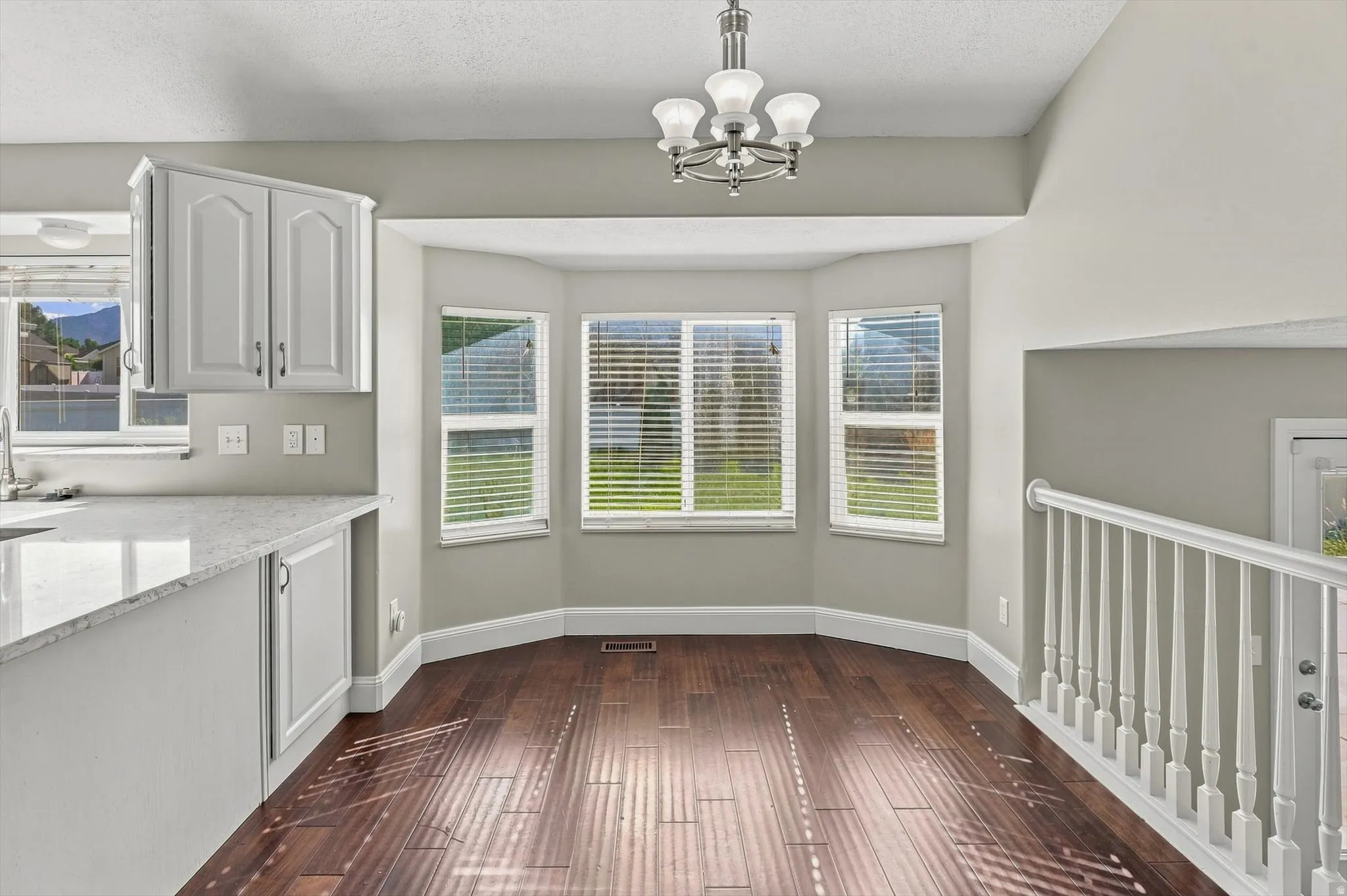 Bay window with natural light, wood-finish flooring, white cabinetry, light-toned countertops, and a white baluster railing