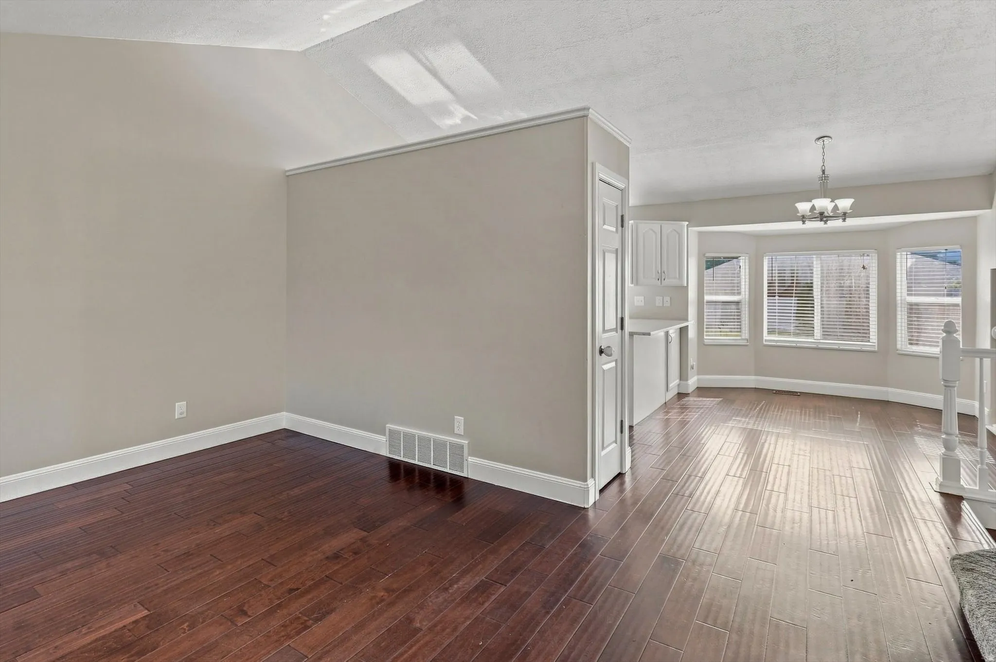Hardwood flooring, painted interior walls, white trim, bay windows, and a built-in chandelier