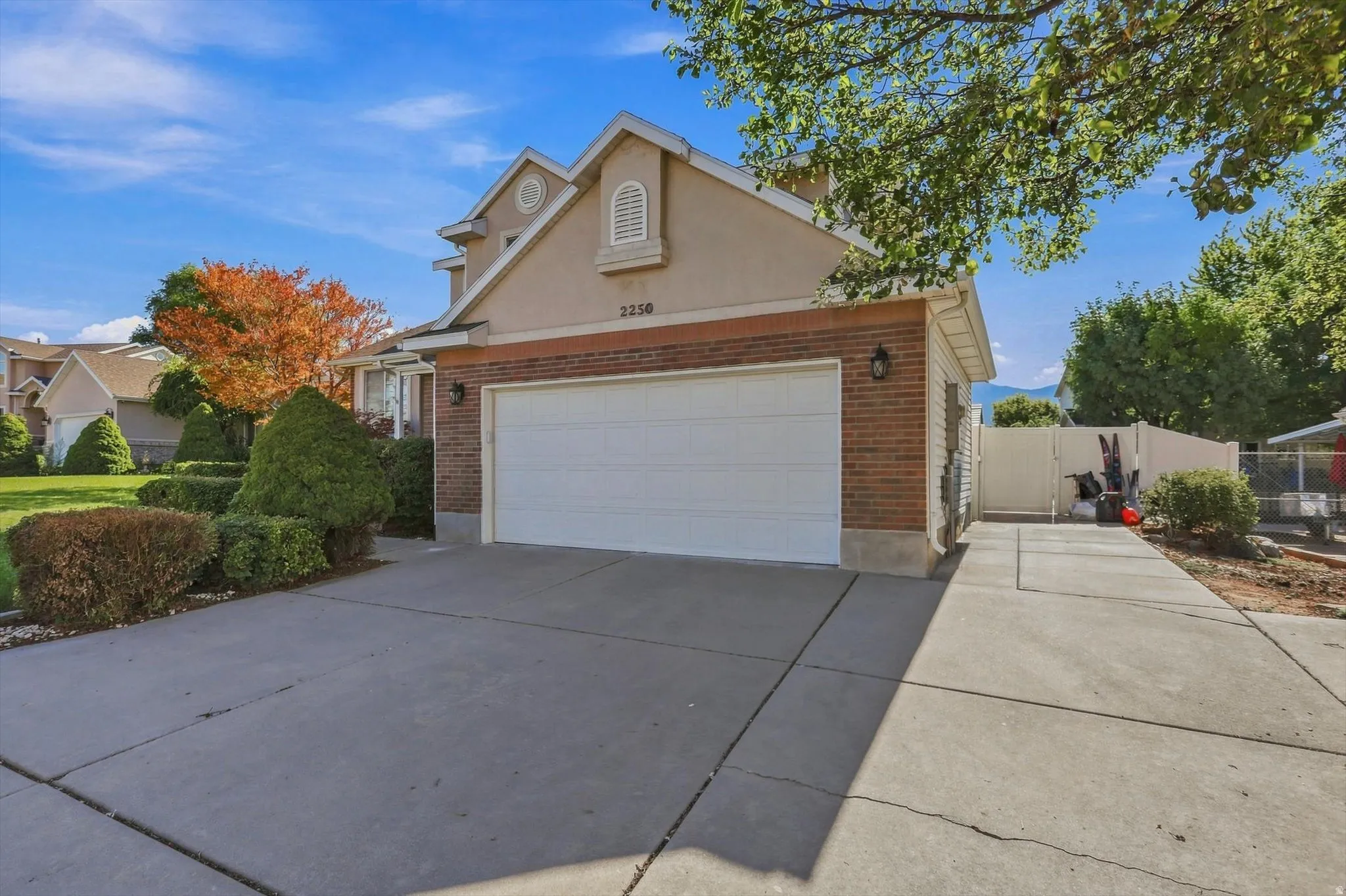 Stucco and brick exterior with a front-facing garage, concrete driveway, and established landscaping