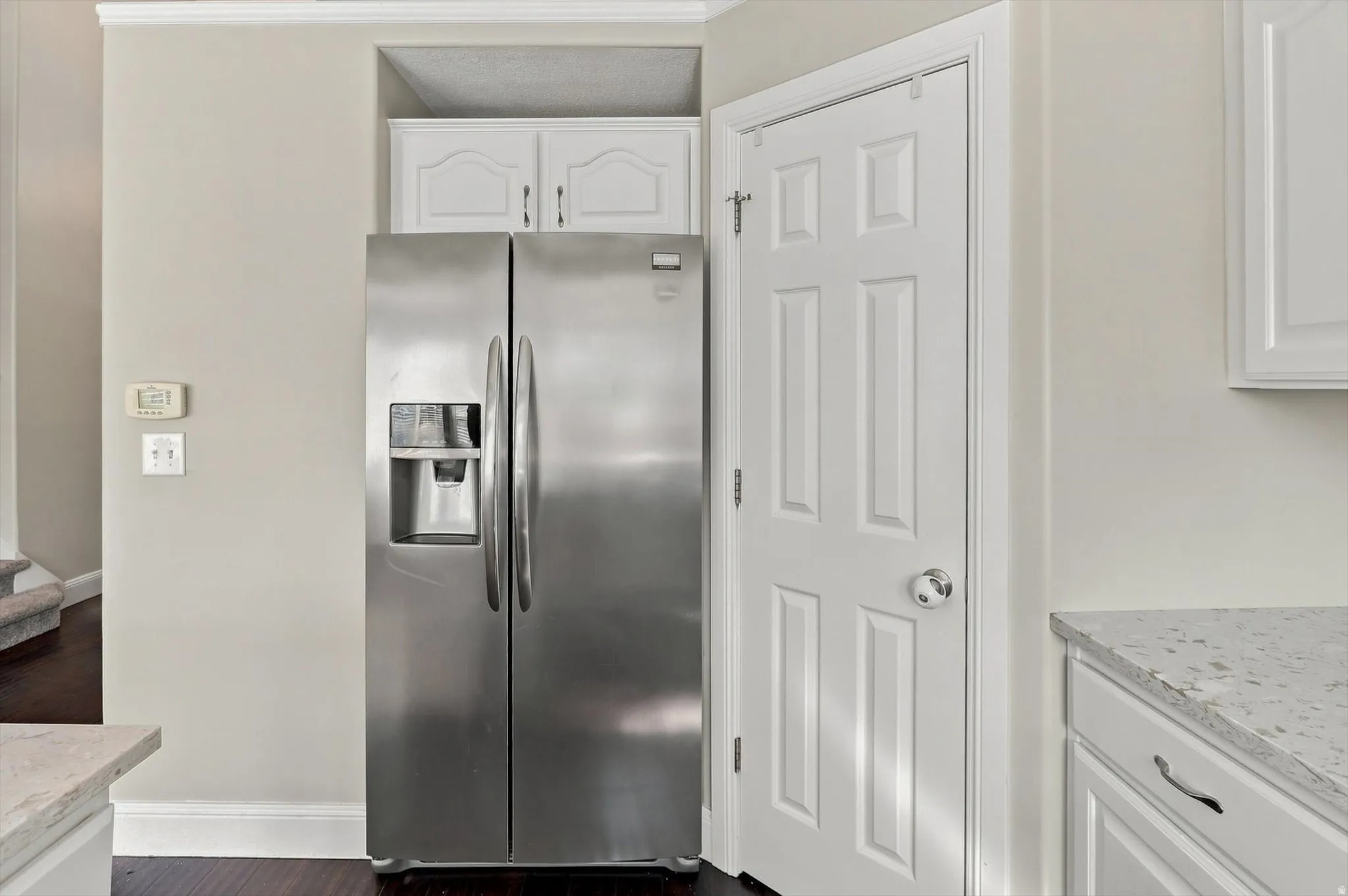 White panel door, white cabinetry, dark wood-finish flooring, and light-toned countertop