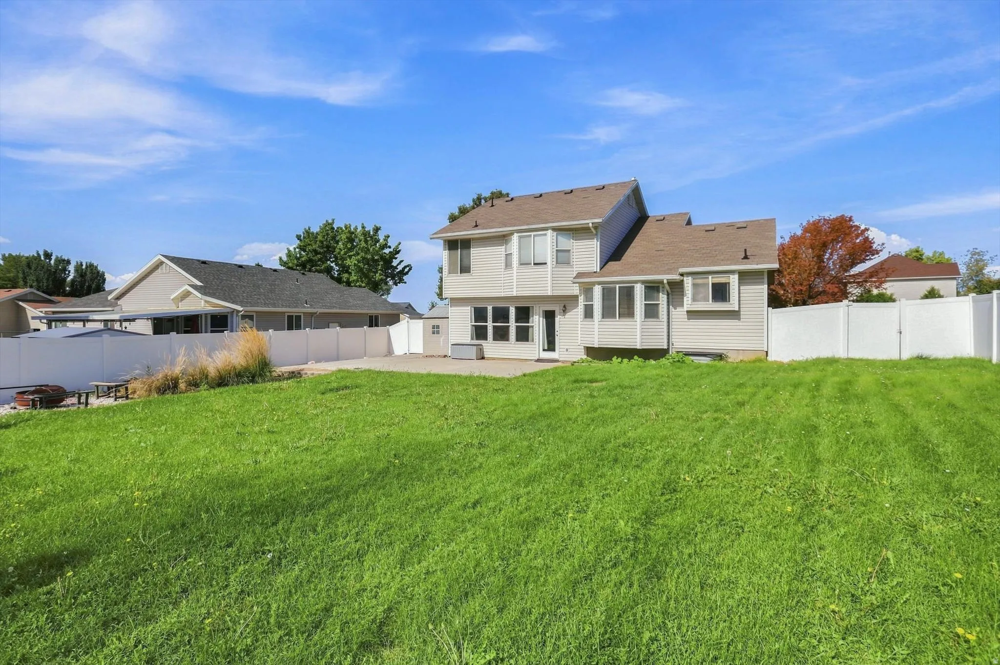 Expansive grassy lawn, concrete patio, white privacy fencing, and exterior siding