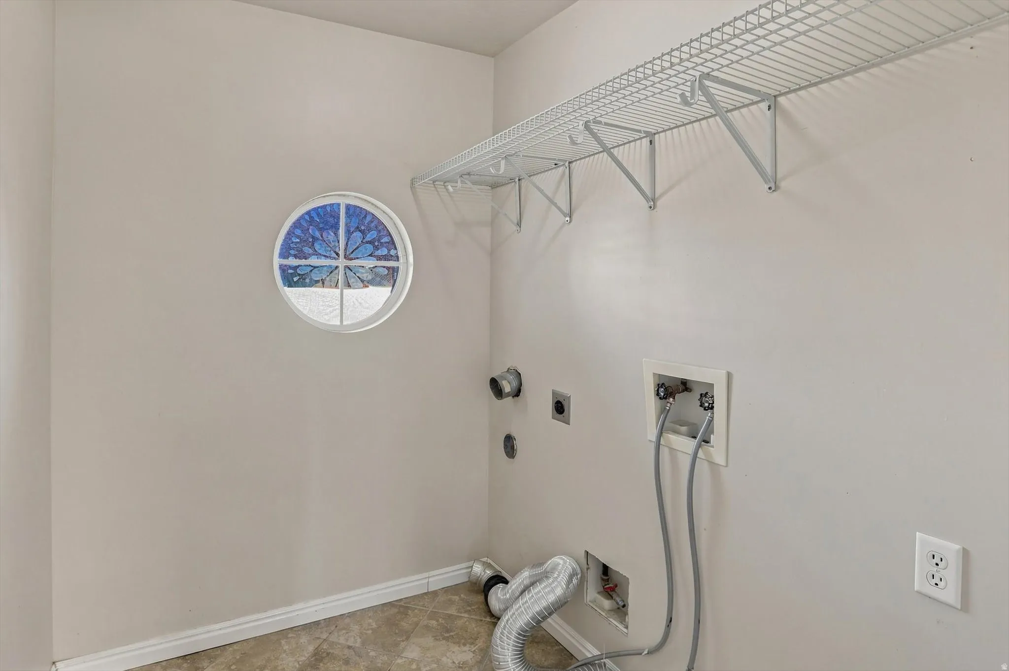 Laundry area featuring tile flooring, a circular stained-glass window, and overhead wire shelving