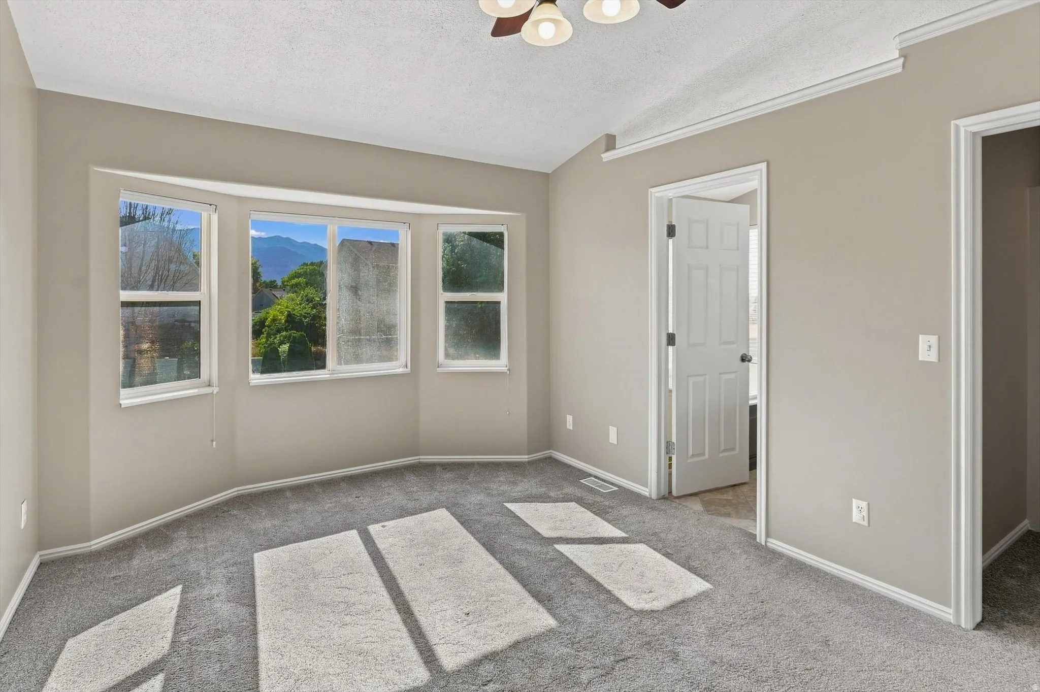 Bay window with multiple panes, ceiling fan light fixture, crown molding, and neutral wall paint