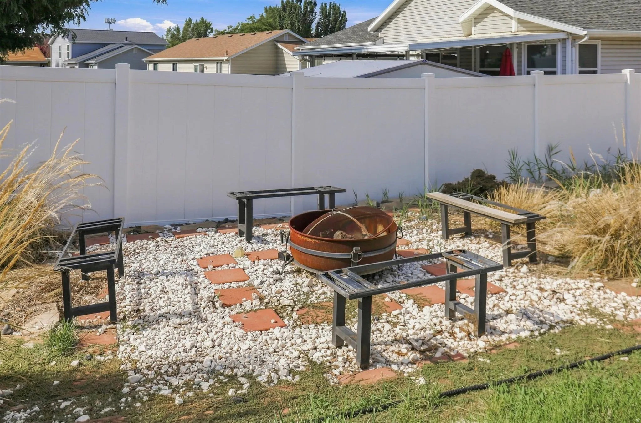 Backyard featuring a white privacy fence, gravel and paver patio, and a metal fire pit
