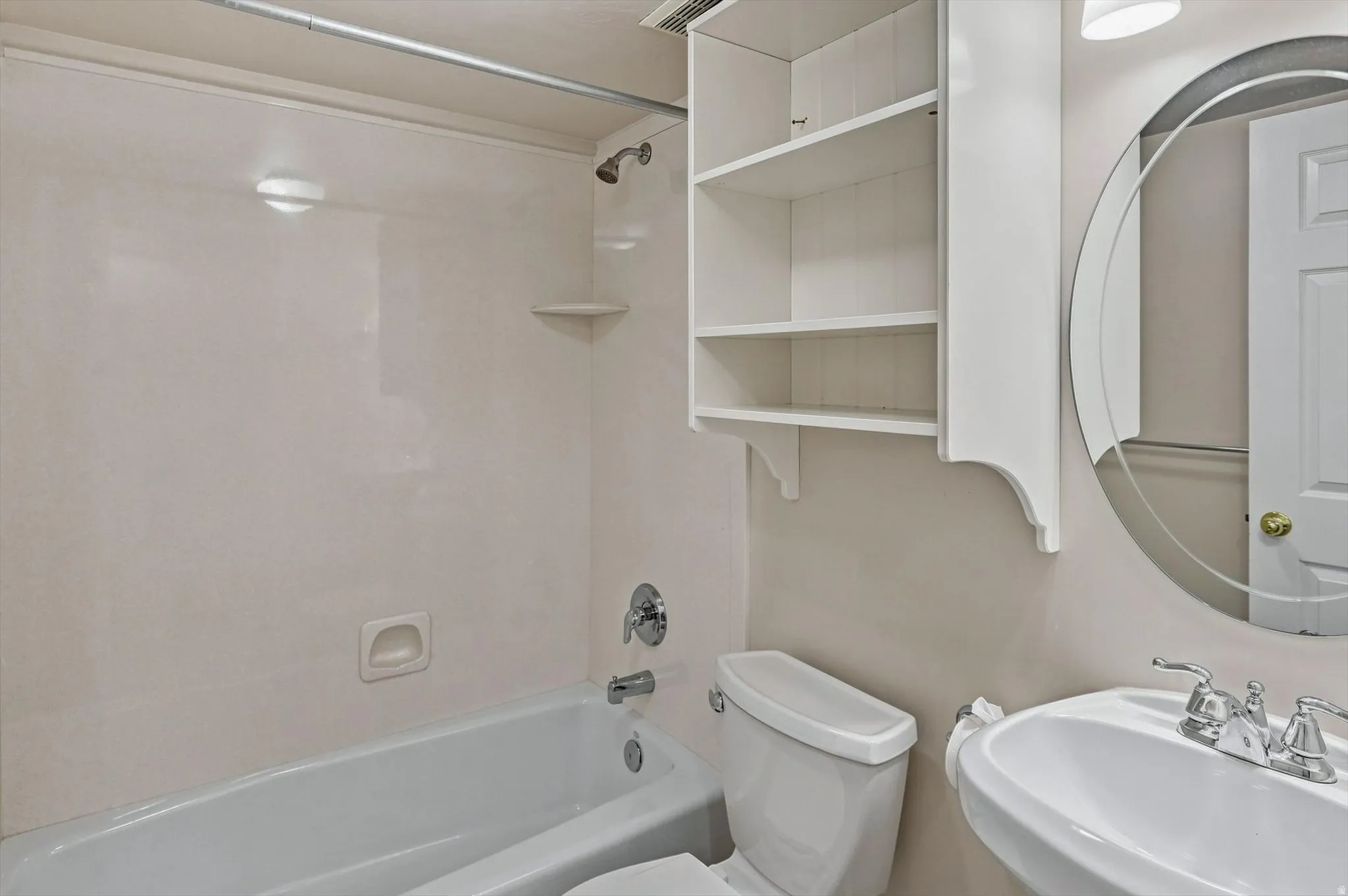White pedestal sink with chrome fixtures, oval mirror, and white wall-mounted shelving