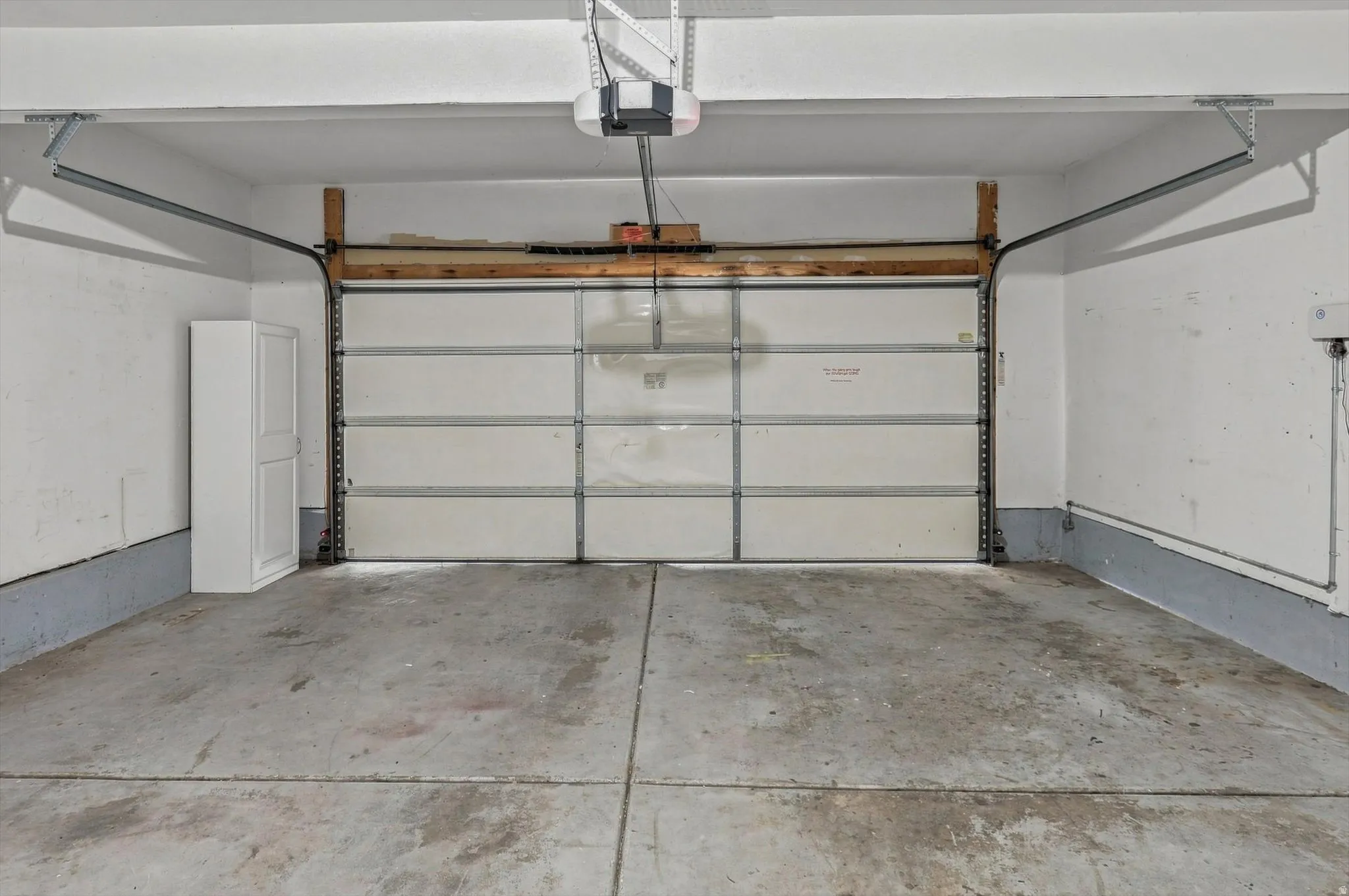 Concrete flooring with painted walls, a segmented garage door, and an overhead garage door opener
