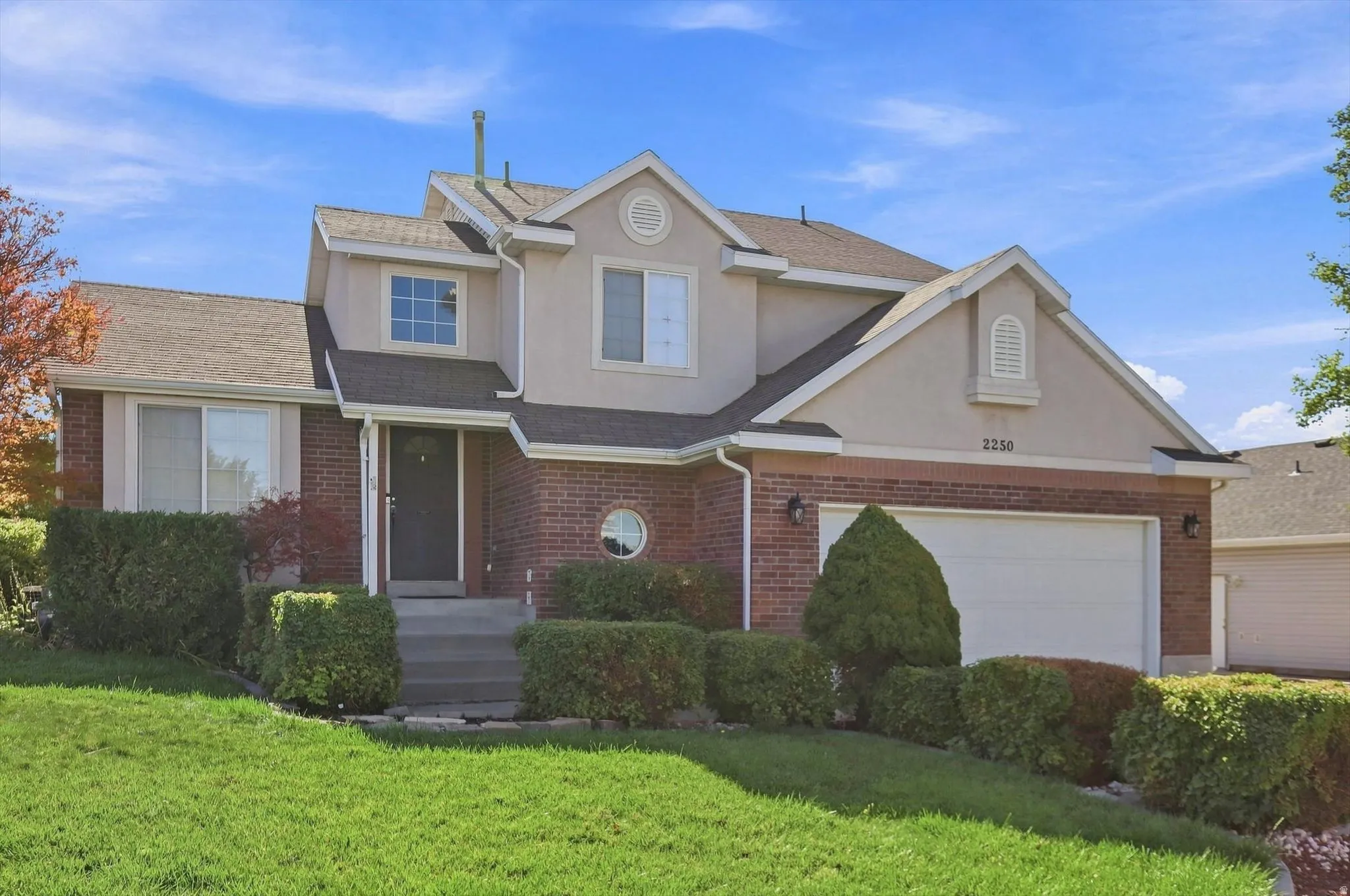 Brick and stucco exterior featuring a gabled roofline, attached garage, and mature landscaping