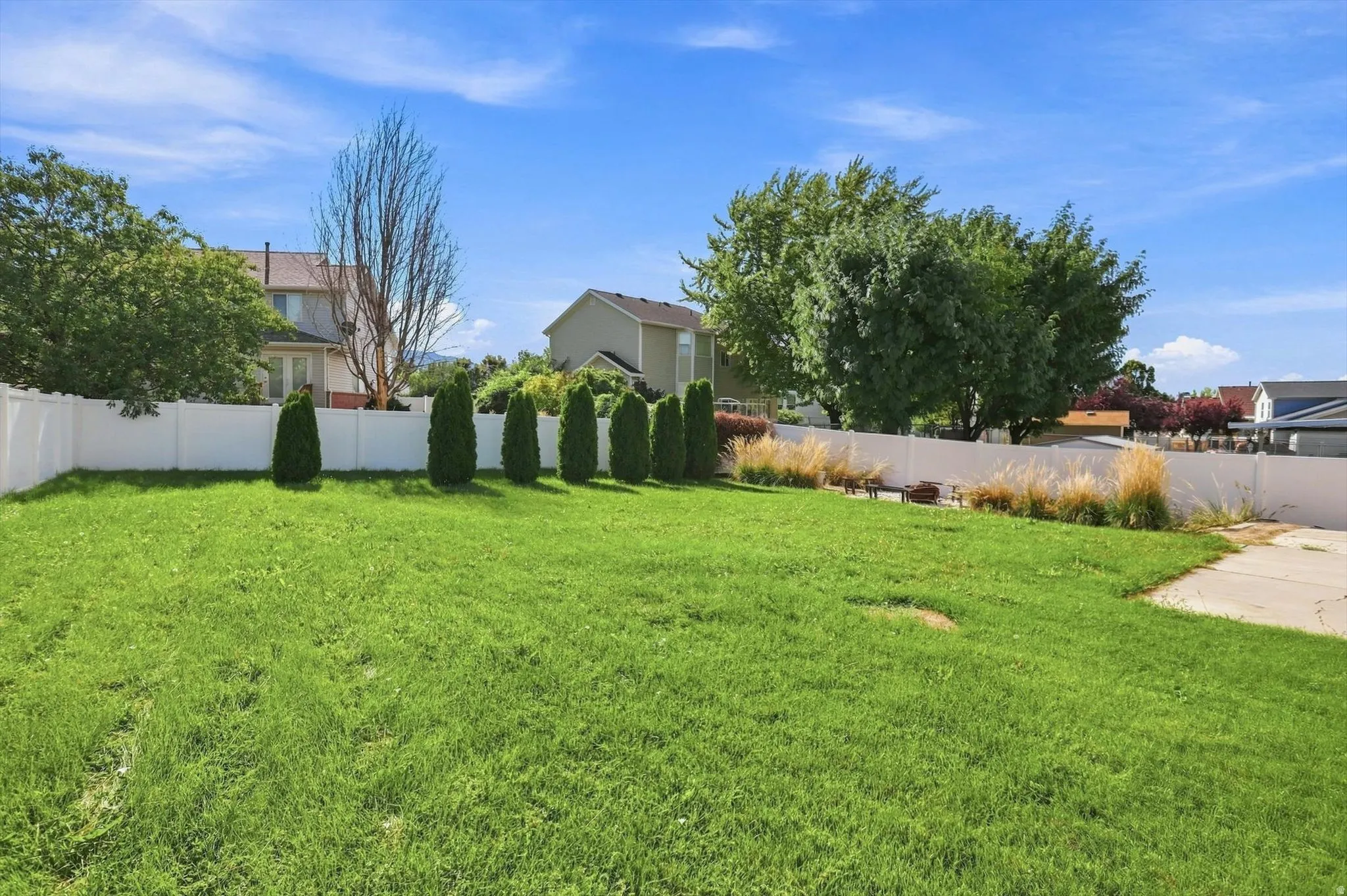 Expansive lawn area featuring a white privacy fence, mature trees, ornamental shrubs, and a concrete pad