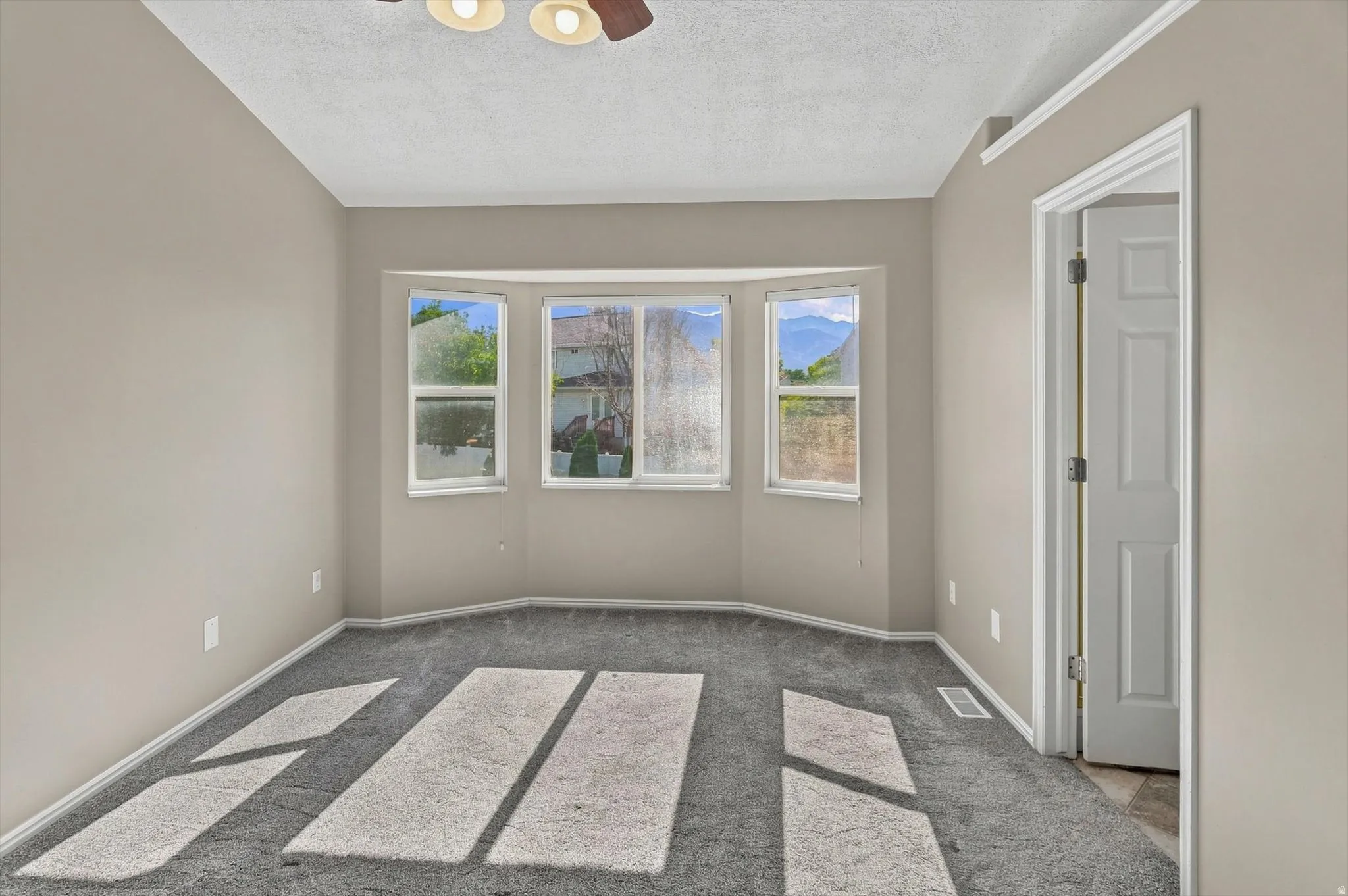 Recessed bay window, gray carpet, neutral wall paint, white trim, ceiling fan