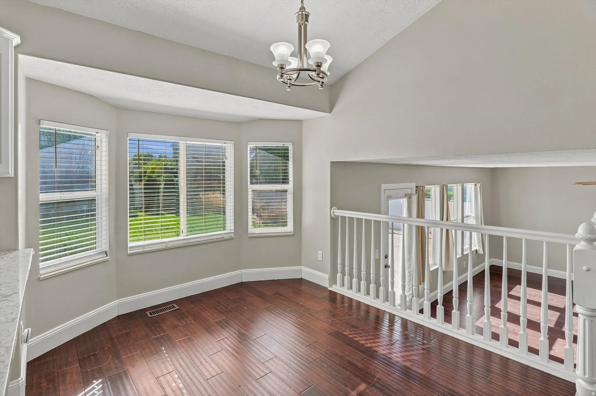 Vaulted ceilings, wood-finish flooring, bay window, white railing, and a brushed nickel chandelier
