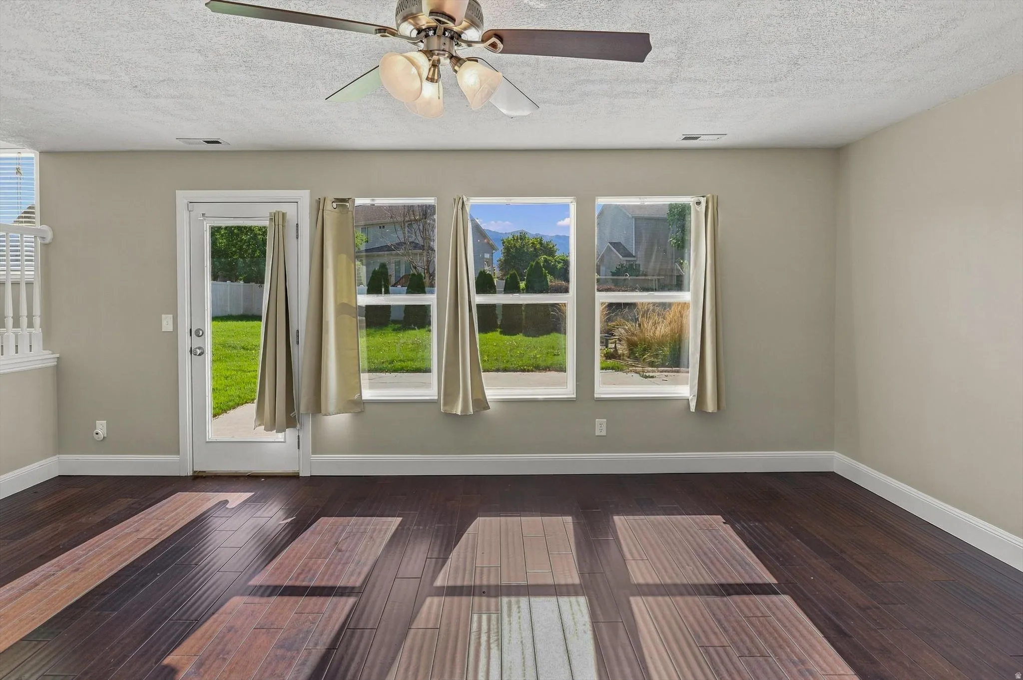 Dark wood-finish flooring, light neutral-toned walls, ceiling fan with integrated lighting, glass-paned door, and multiple windows