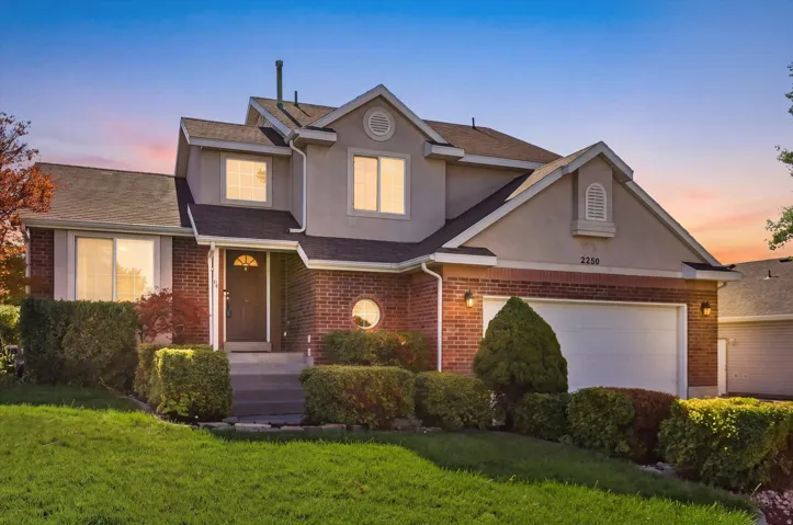 Stucco and brick exterior with a two-car garage, established front landscaping, and a covered entry