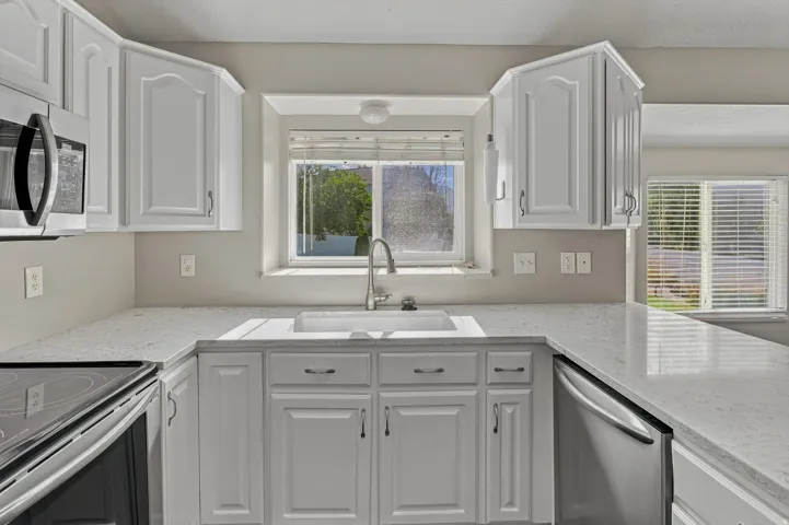 White cabinetry with brushed nickel hardware, stainless steel appliances, a double basin sink, and light-toned countertops