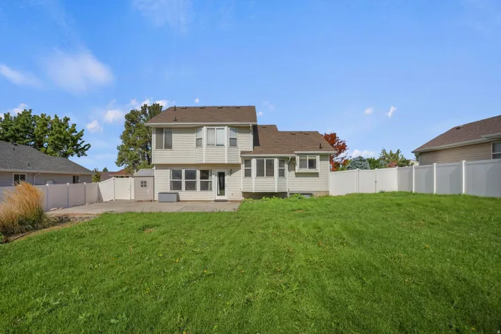 Expansive backyard featuring a manicured lawn, concrete patio, and white privacy fencing