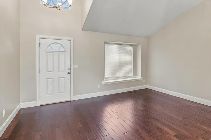 Hardwood-finish flooring throughout, a vaulted ceiling, and a prominent front entry door with an arched window accent