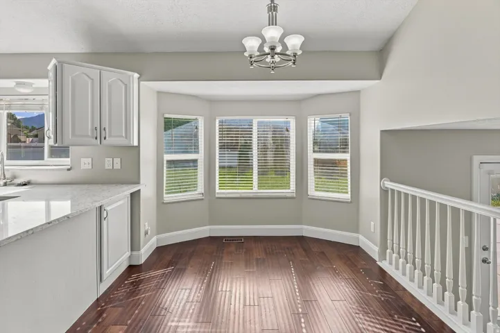 Bay window with natural light, wood-finish flooring, white cabinetry, light-toned countertops, and a white baluster railing