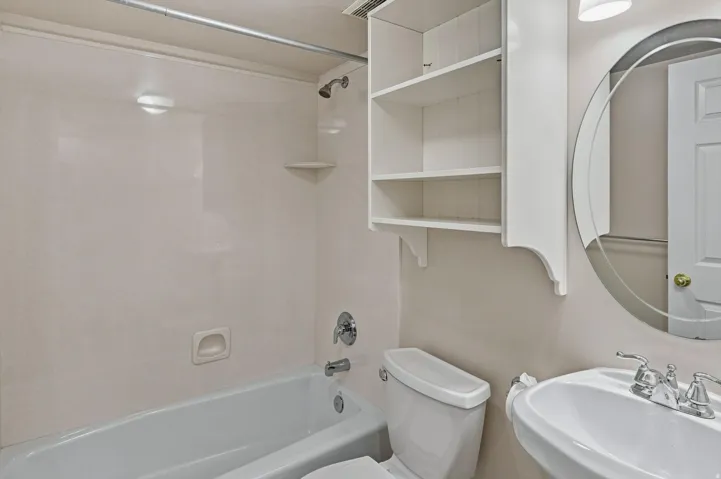 White pedestal sink with chrome fixtures, oval mirror, and white wall-mounted shelving
