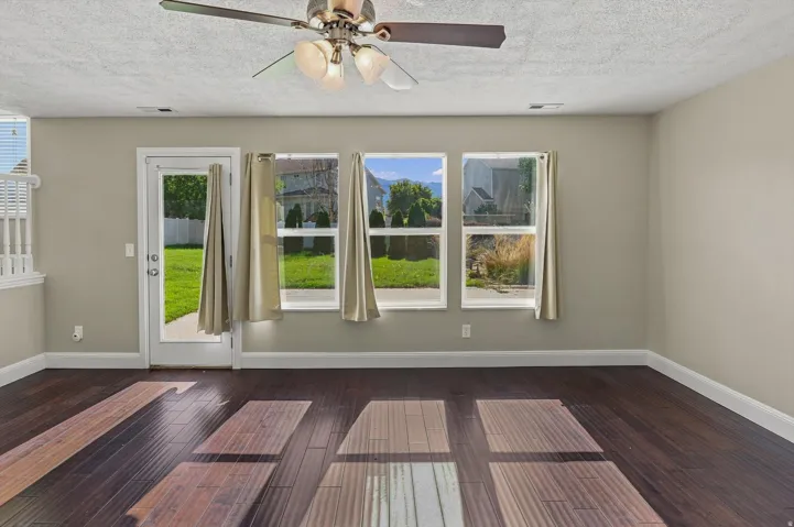Dark wood-finish flooring, light neutral-toned walls, ceiling fan with integrated lighting, glass-paned door, and multiple windows