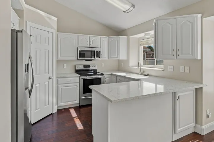 Bright, open kitchen featuring white cabinetry with raised-panel doors, stainless steel appliances including a microwave and electric range, quartz countertops, a center island with additional counter space, and wood-finish flooring throughout