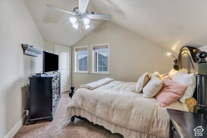 Bright upper-level bedroom featuring vaulted ceilings with ceiling fan, dual windows with plantation shutters, wood-finish flooring, and built-in dresser with mirror and attached lighting fixtures
