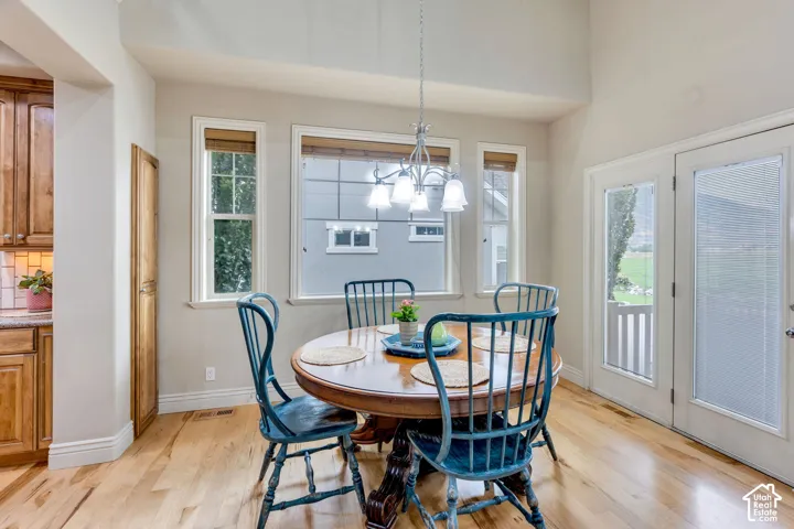 Vaulted ceiling with an attached chandelier, wood-finish flooring, multiple windows providing natural illumination, and a double patio door