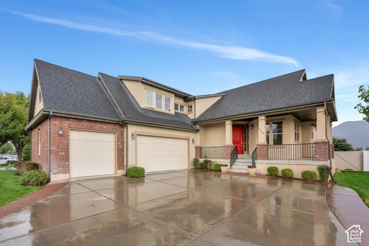 Stucco and brick exterior with a prominent covered porch, dual garage doors, and a paved driveway
