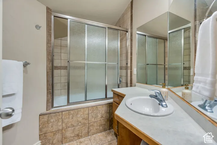 Master bathroom featuring a circular vessel sink set in a wood-finish vanity with quartz countertop, frameless glass shower enclosure with tile surround, and dual mirrors with integrated lighting