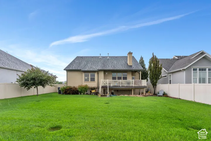 Expansive backyard featuring a manicured lawn, a raised deck with white railings, and a stucco exterior