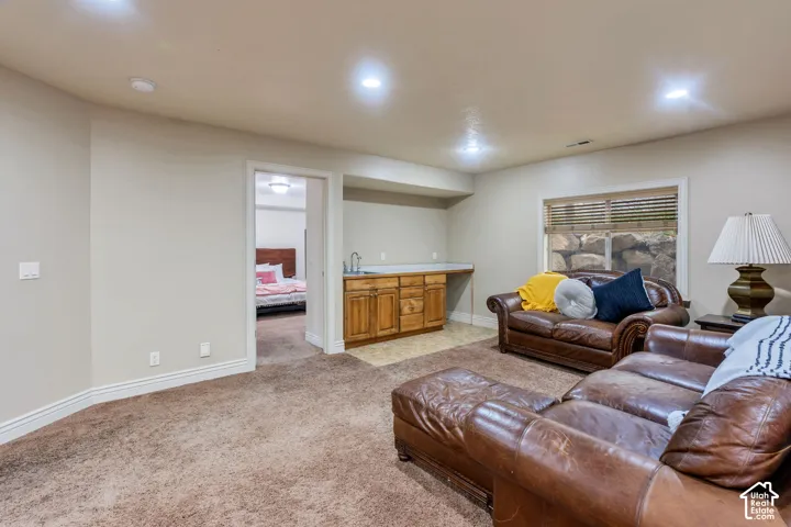 Carpeted living area with recessed lighting, a wet bar featuring wood cabinetry, and a window with horizontal blinds