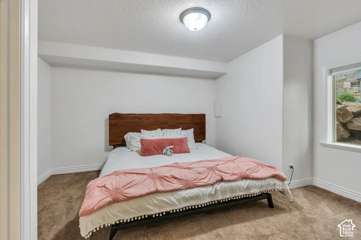 White walls with textured ceilings, brown carpet, window with white trim, and a semi-flush mount ceiling light