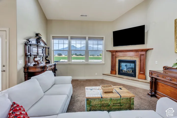 Living space featuring vaulted ceilings, a built-in fireplace with a wood mantel, multiple windows, and carpet flooring