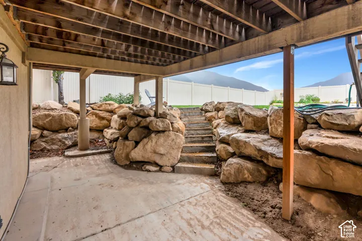Covered patio area with concrete surfacing, exposed wood beam ceiling, stone retaining walls, and concrete steps
