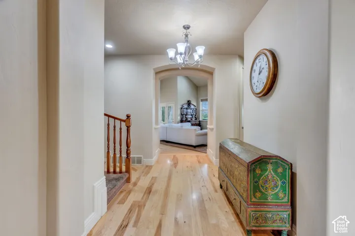 Hardwood flooring, arched entryway, staircase with wood banister, chandelier lighting, recessed lighting