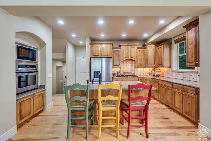 Kitchen featuring wood-finish flooring, built-in stainless steel appliances, a center island with countertop, natural wood cabinetry, and a subway tile backsplash